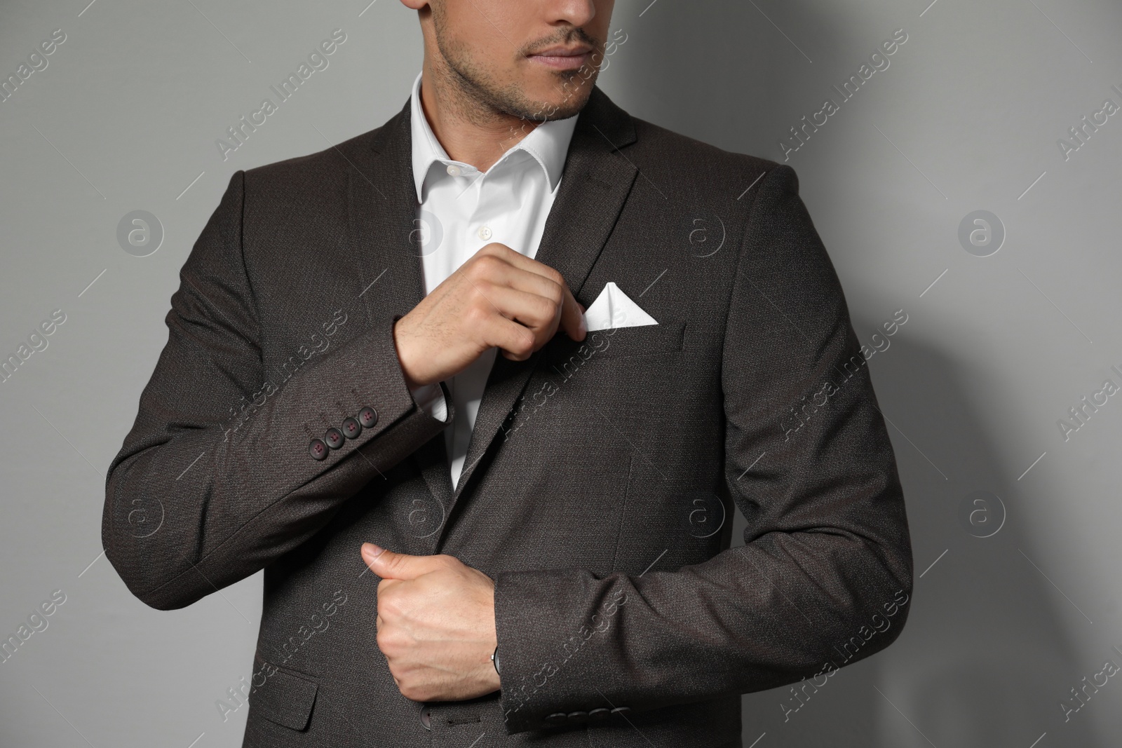 Photo of Man fixing handkerchief in breast pocket of his suit on light grey background, closeup