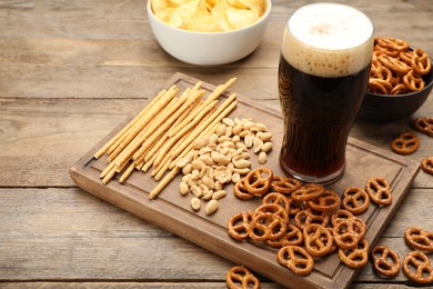 Photo of Glass of beer served with delicious pretzel crackers and other snacks on wooden table