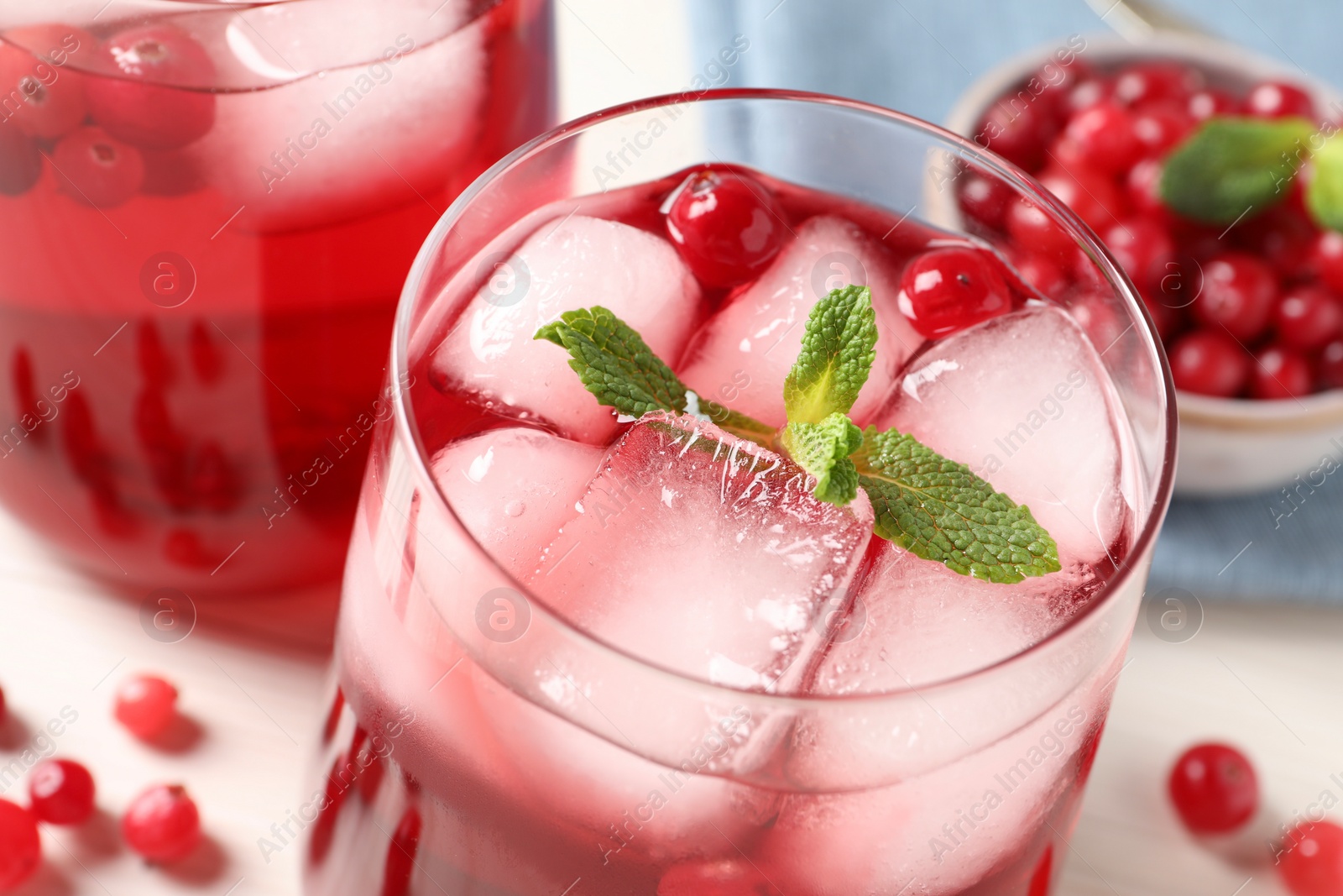 Photo of Tasty cranberry juice with ice cubes in glasses and fresh berries on white table, closeup