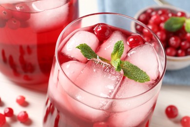 Tasty cranberry juice with ice cubes in glasses and fresh berries on white table, closeup