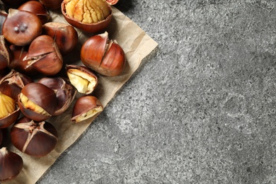 Photo of Delicious roasted edible chestnuts on grey table, flat lay. Space for text
