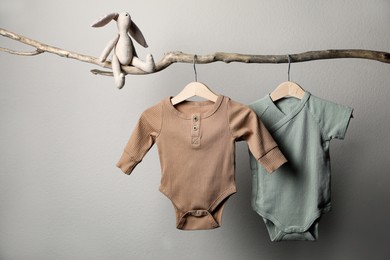 Photo of Baby bodysuits and toy on decorative branch near light wall
