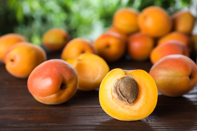 Many fresh ripe apricots on wooden table against blurred background