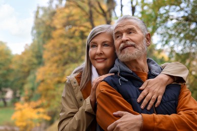 Portrait of affectionate senior couple in autumn park, space for text