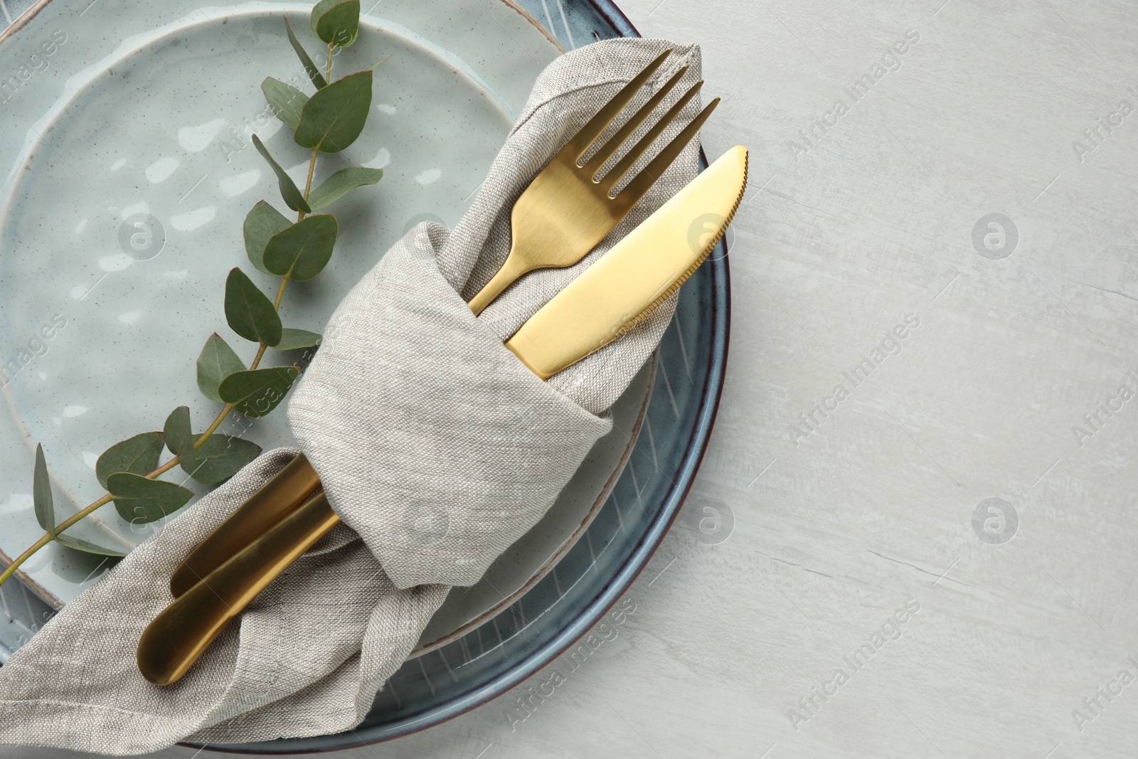 Photo of Stylish setting with cutlery, napkin, eucalyptus branch and plates on white table, top view. Space for text