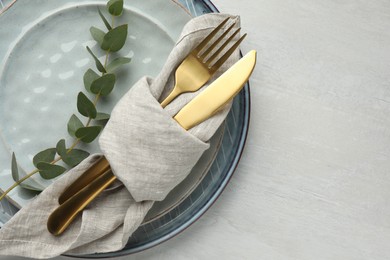 Stylish setting with cutlery, napkin, eucalyptus branch and plates on white table, top view. Space for text