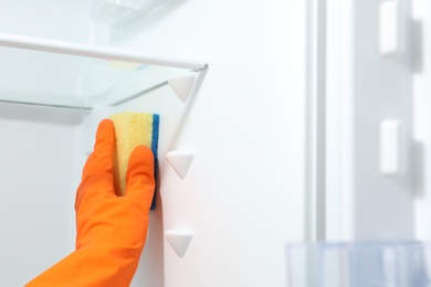 Photo of Worker in rubber gloves cleaning empty refrigerator, closeup