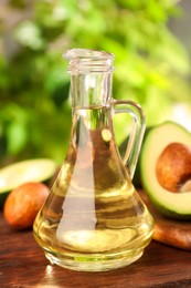 Photo of Glass jugcooking oil and fresh avocados on wooden table against blurred green background
