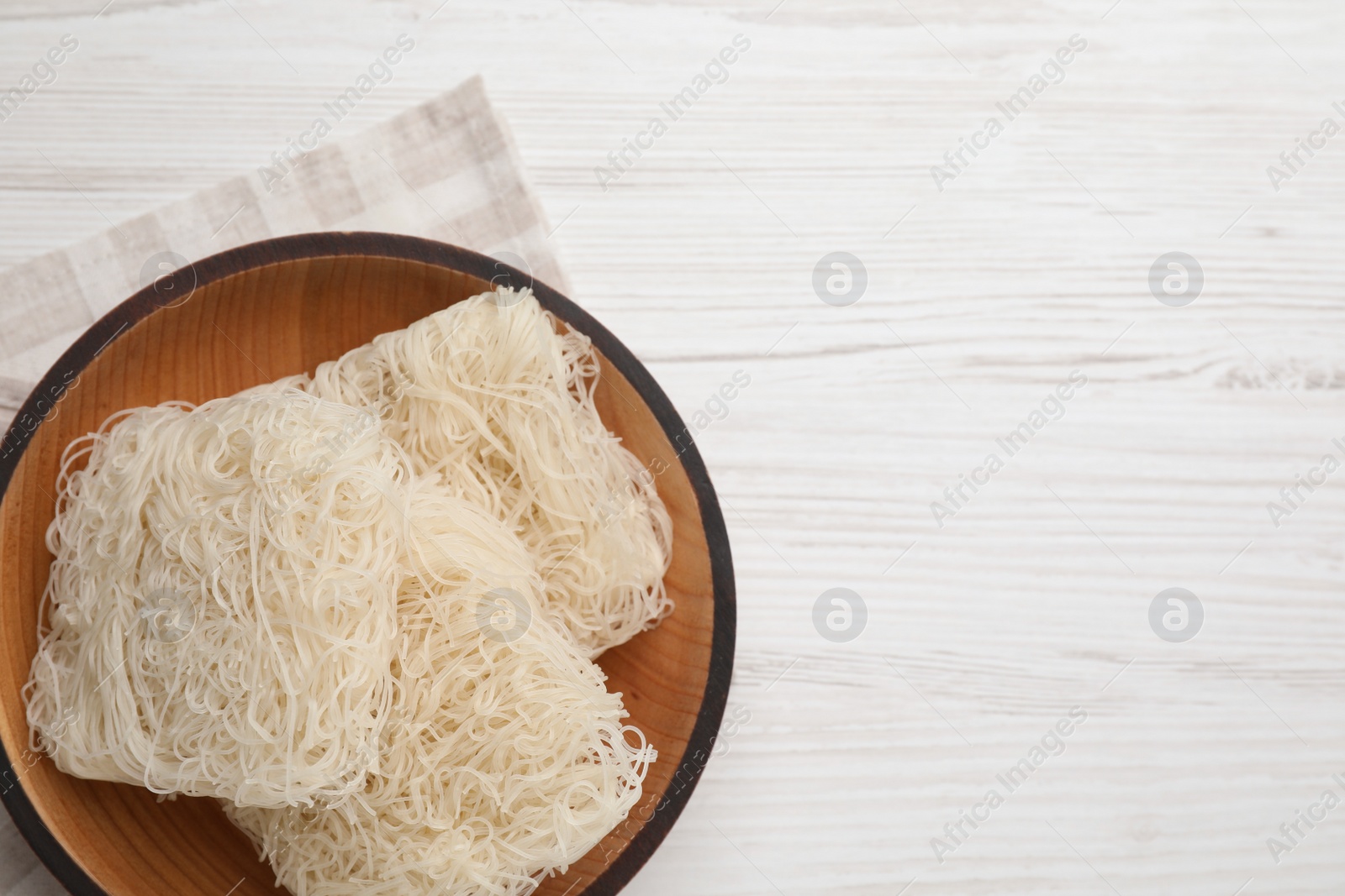 Photo of Bowl with dried rice noodles and napkin on white wooden table, top view. Space for text