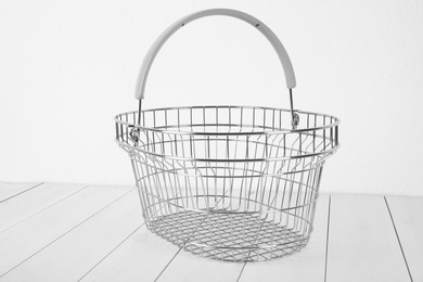 Empty metal shopping basket on light wooden table against white background