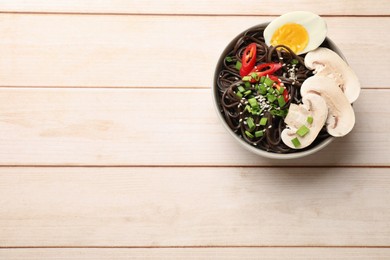 Photo of Tasty buckwheat noodles (soba) with mushrooms, egg and chili pepper in bowl on wooden table, top view. Space for text