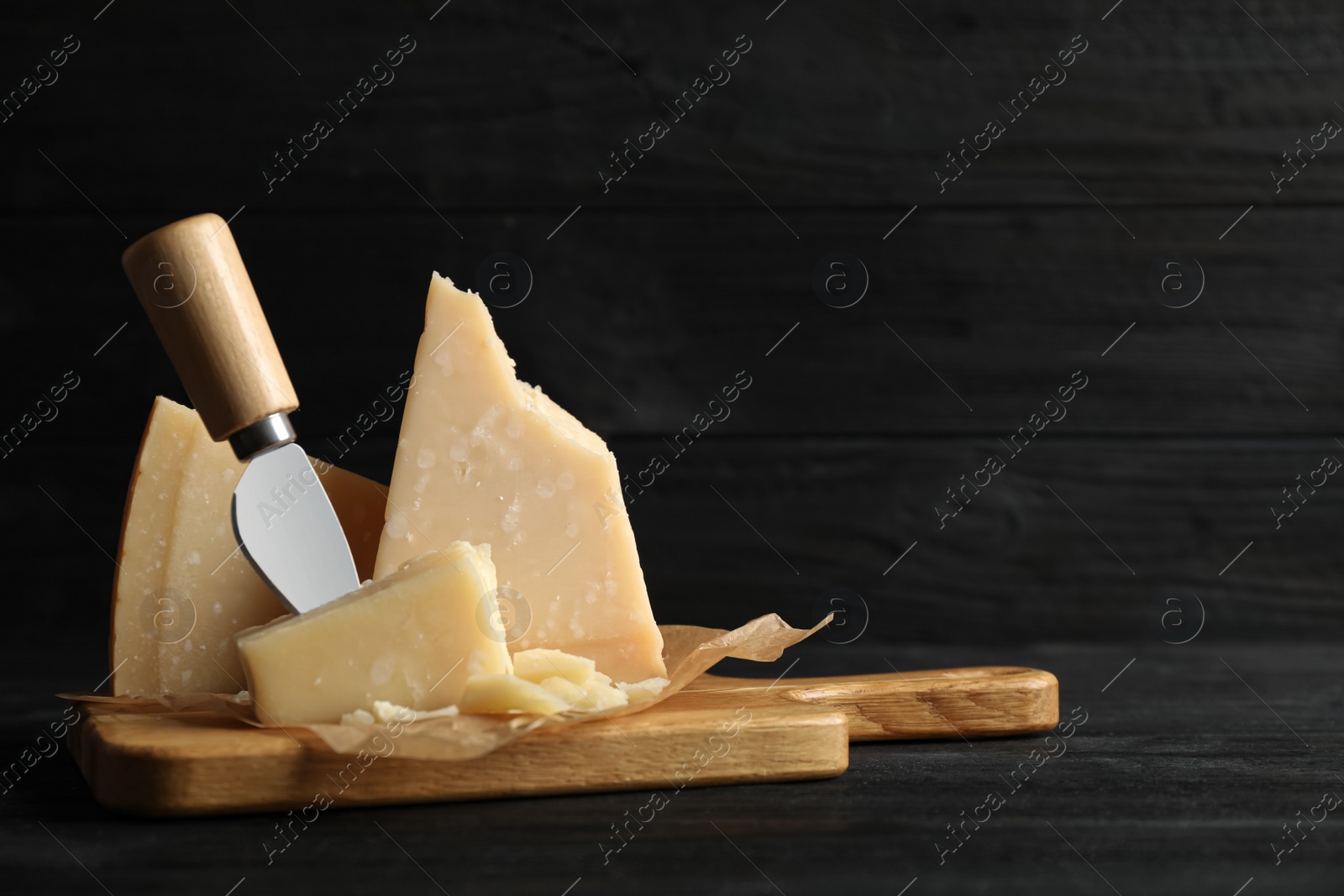 Photo of Pieces of Parmesan cheese and knife on black wooden table. Space for text