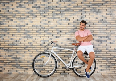 Photo of Handsome young hipster man with bicycle near brick wall