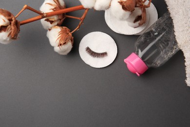 Bottle of makeup remover, cotton flowers, pads, towel and false eyelashes on grey background, flat lay. Space for text