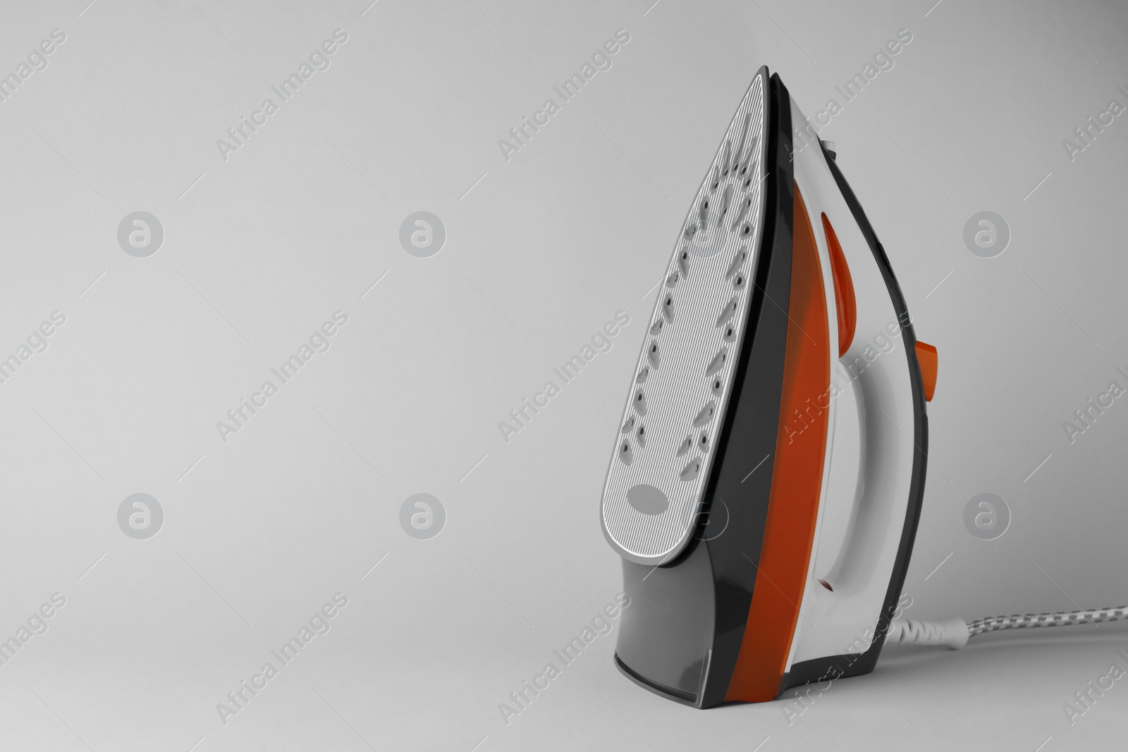 Photo of One modern iron on light grey background, space for text. Home appliance
