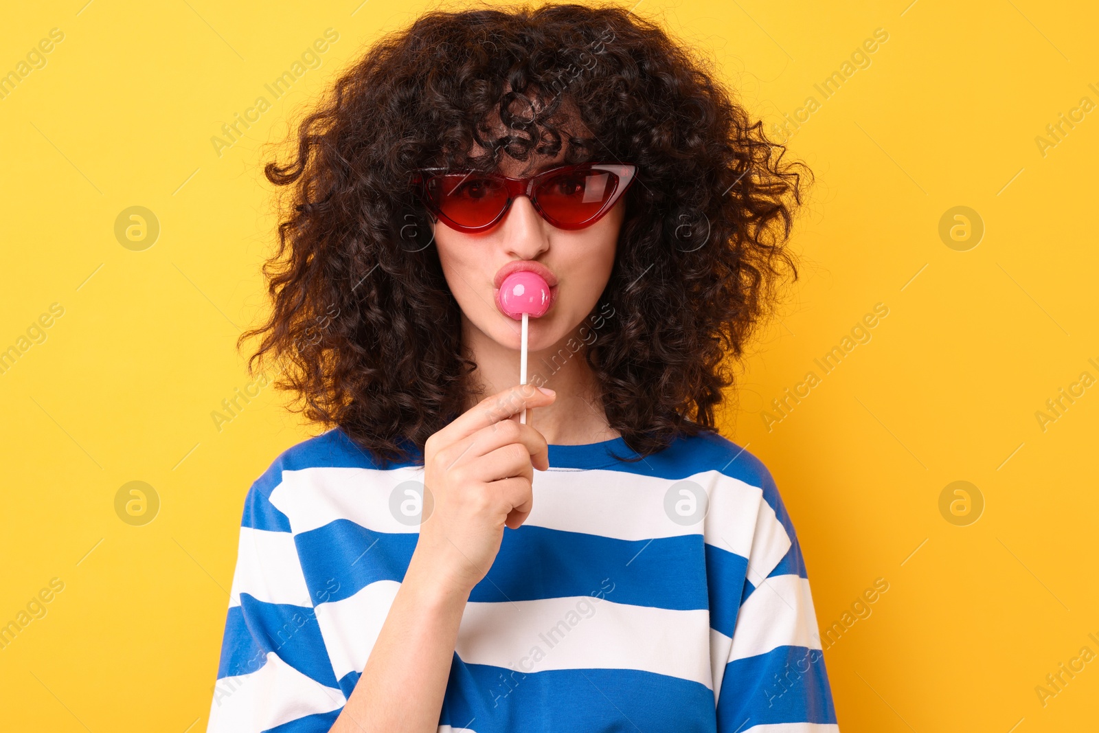 Photo of Beautiful woman in sunglasses with lollipop on yellow background