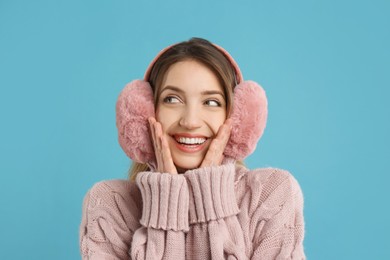 Happy woman wearing warm earmuffs on light blue background