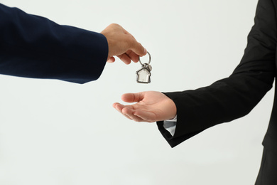 Photo of Real estate agent giving key to client on light background, closeup