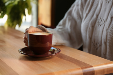 Woman with aromatic coffee at table in cafe, closeup