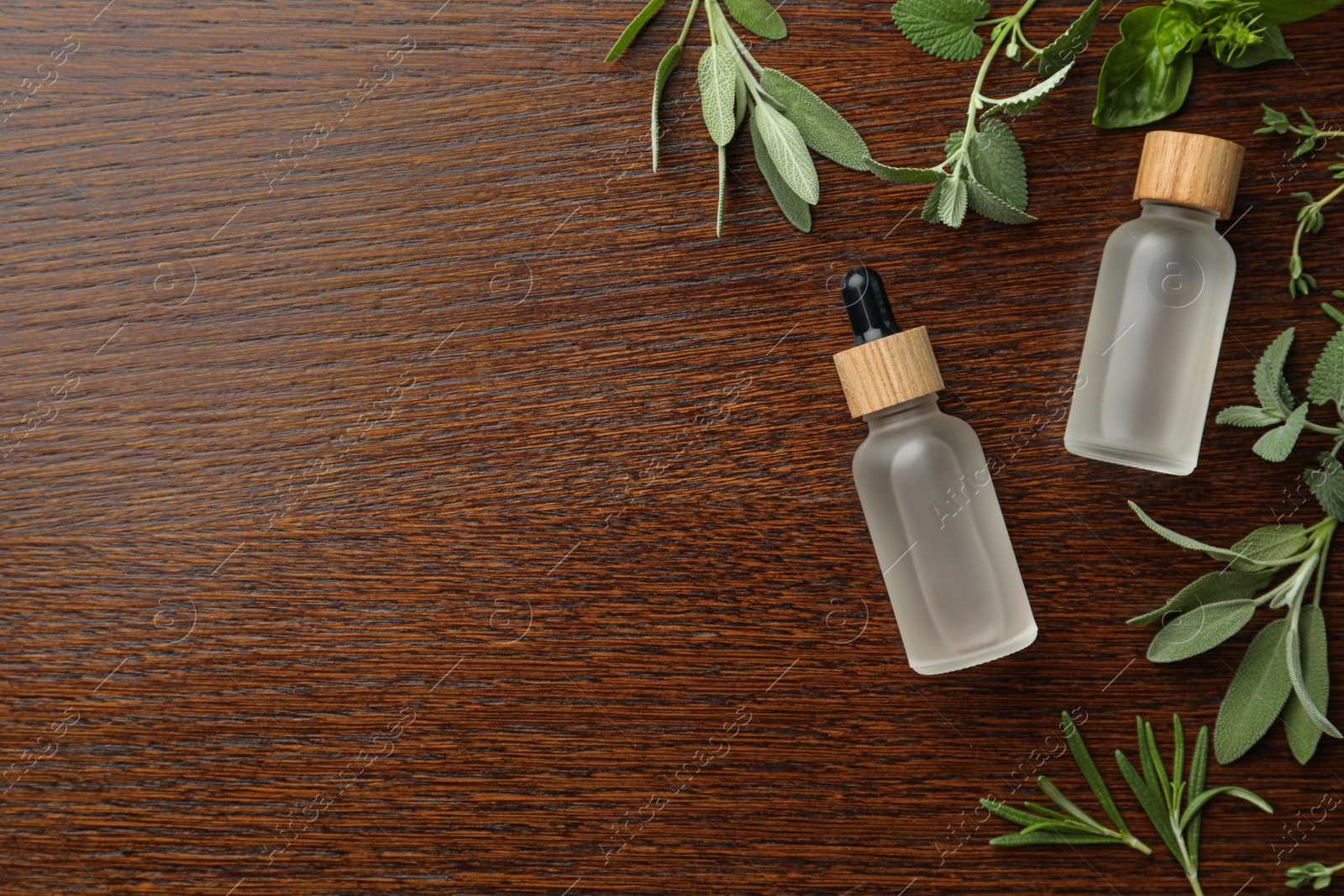 Photo of Bottles of essential oil and fresh herbs on wooden table, flat lay. Space for text