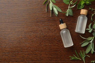 Bottles of essential oil and fresh herbs on wooden table, flat lay. Space for text