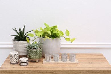 Photo of Stylish decor with houseplants on wooden table near white wall. Interior design