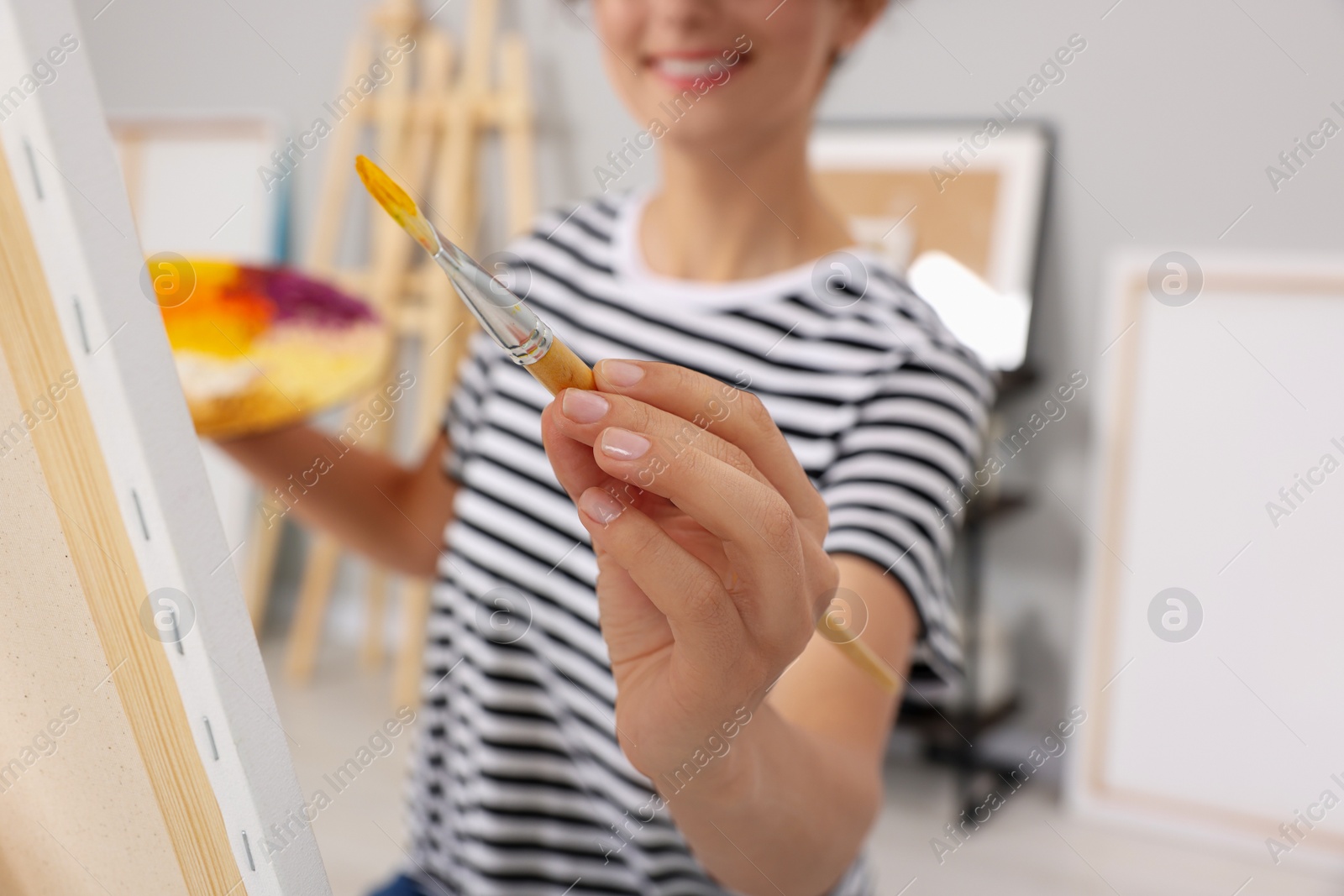 Photo of Young woman painting on easel with canvas in studio, closeup