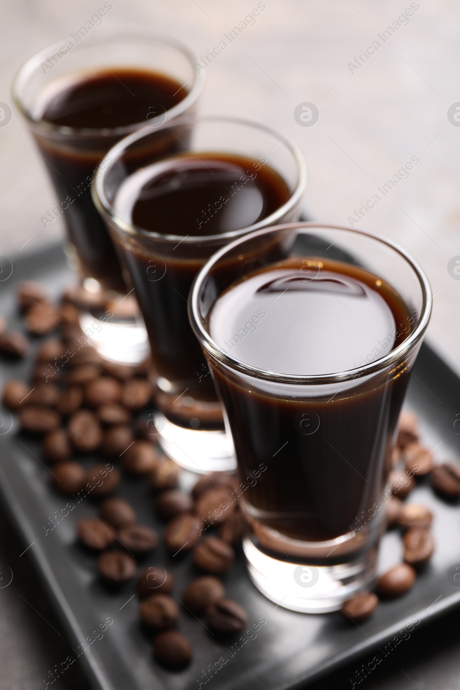 Photo of Shot glasses with coffee liqueur and beans on light grey table, closeup