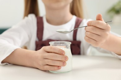 Cute little girl with tasty yogurt at white table, closeup