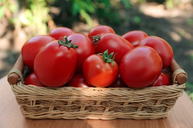 Wicker basket with fresh tomatoes on wooden table outdoors, closeup