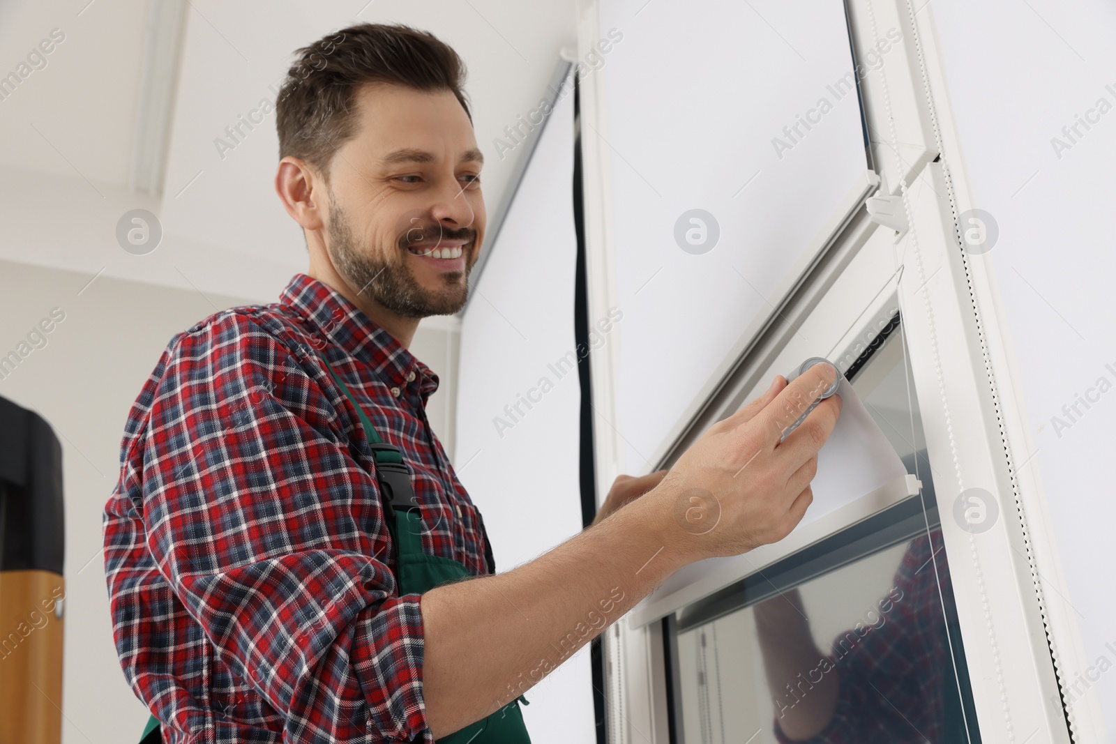 Photo of Worker in uniform installing roller window blind indoors