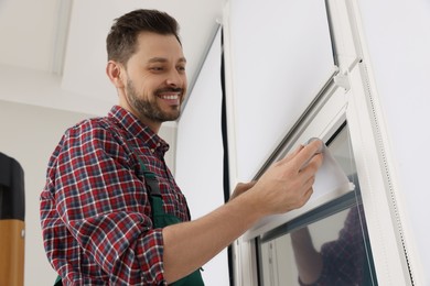 Photo of Worker in uniform installing roller window blind indoors