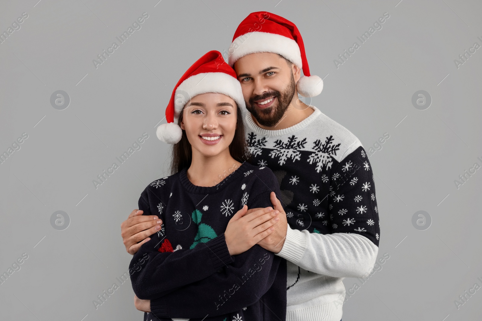 Photo of Happy young couple in Christmas sweaters and Santa hats on grey background