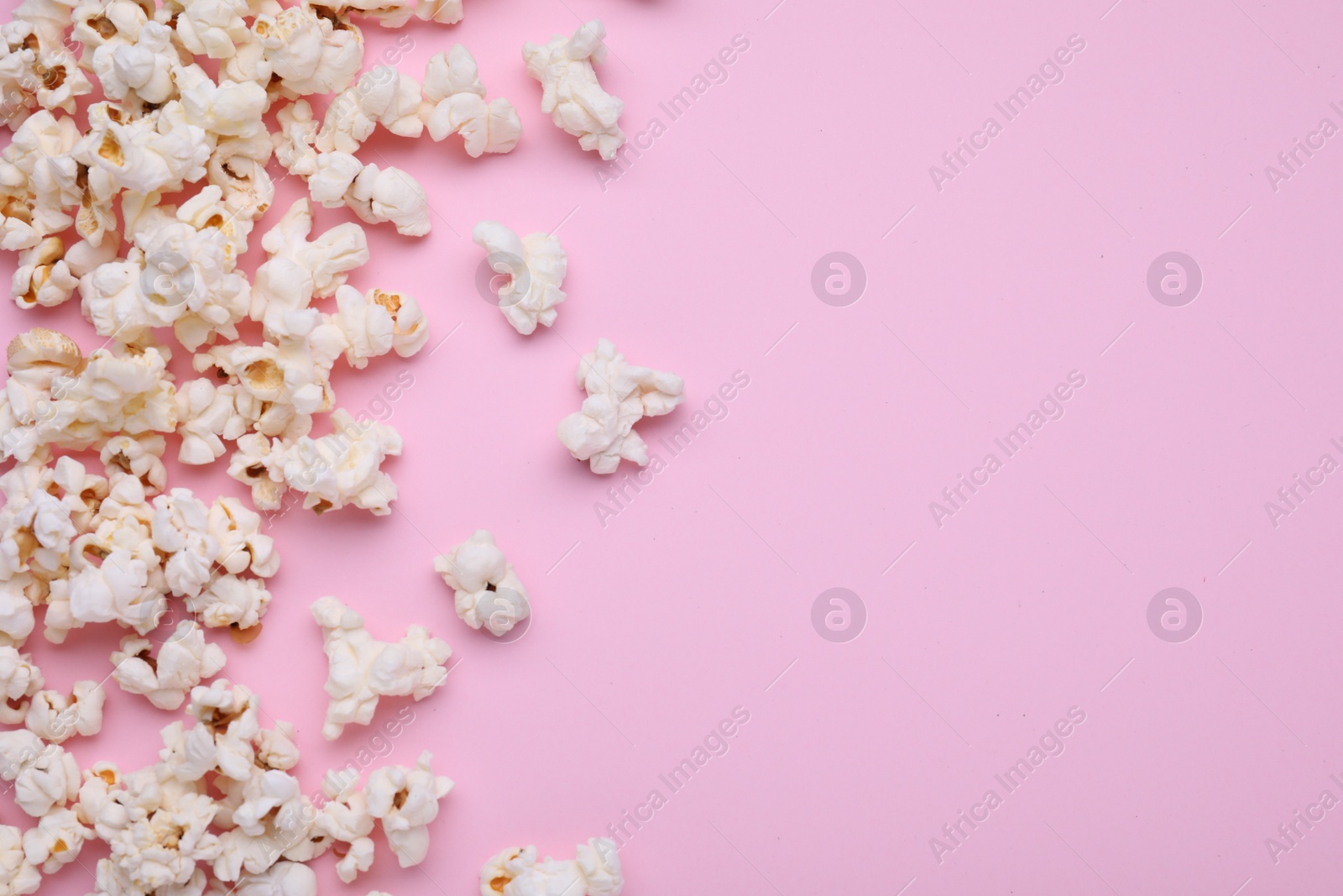 Photo of Tasty popcorn scattered on pink background, flat lay. Space for text