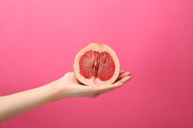 Photo of Woman holding half of grapefruit on pink background, closeup. Sex concept