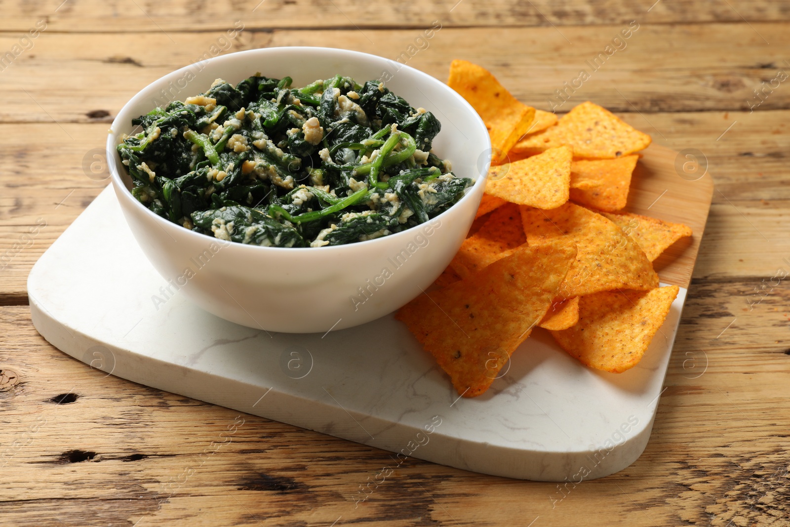 Photo of Tasty spinach dip with eggs in bowl and nachos chips on wooden table