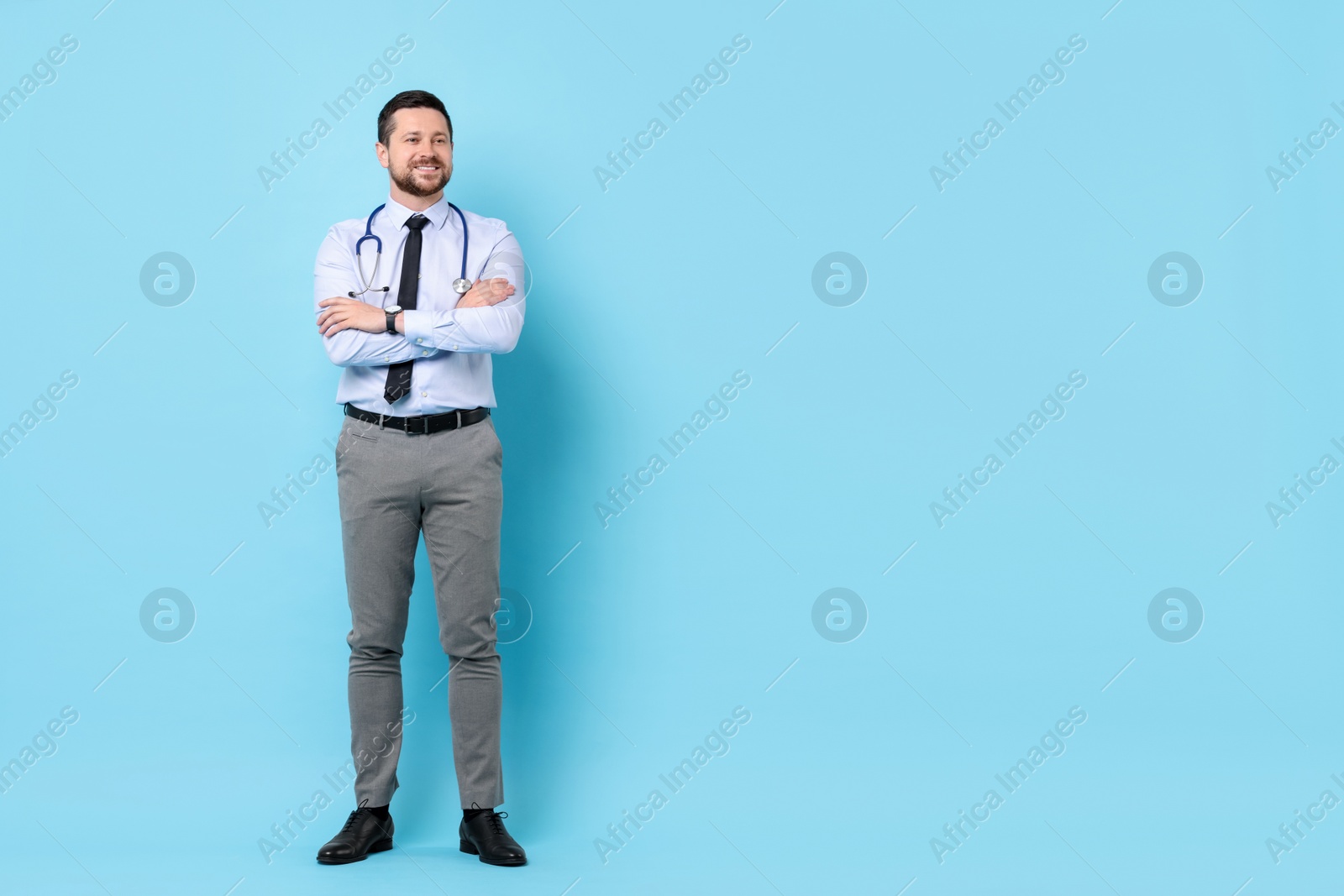 Photo of Smiling doctor with stethoscope on light blue background. Space for text