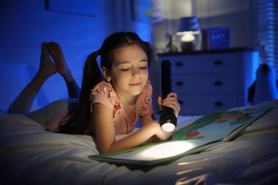 Photo of Little girl with flashlight reading fairy tale in dark bedroom