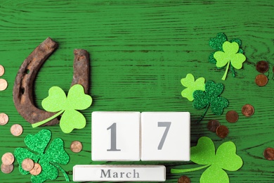 Flat lay composition with horseshoe and block calendar on green wooden background. St. Patrick's Day celebration