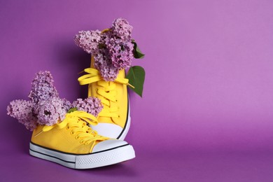 Photo of Bright yellow canvas shoes with beautiful lilac on purple background, space for text