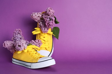 Bright yellow canvas shoes with beautiful lilac on purple background, space for text