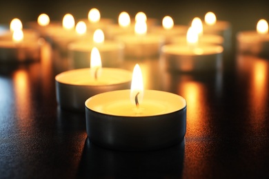 Wax candles burning on table in darkness, closeup