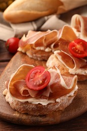 Photo of Board of tasty sandwiches with cured ham, tomato and cream cheese on table, closeup