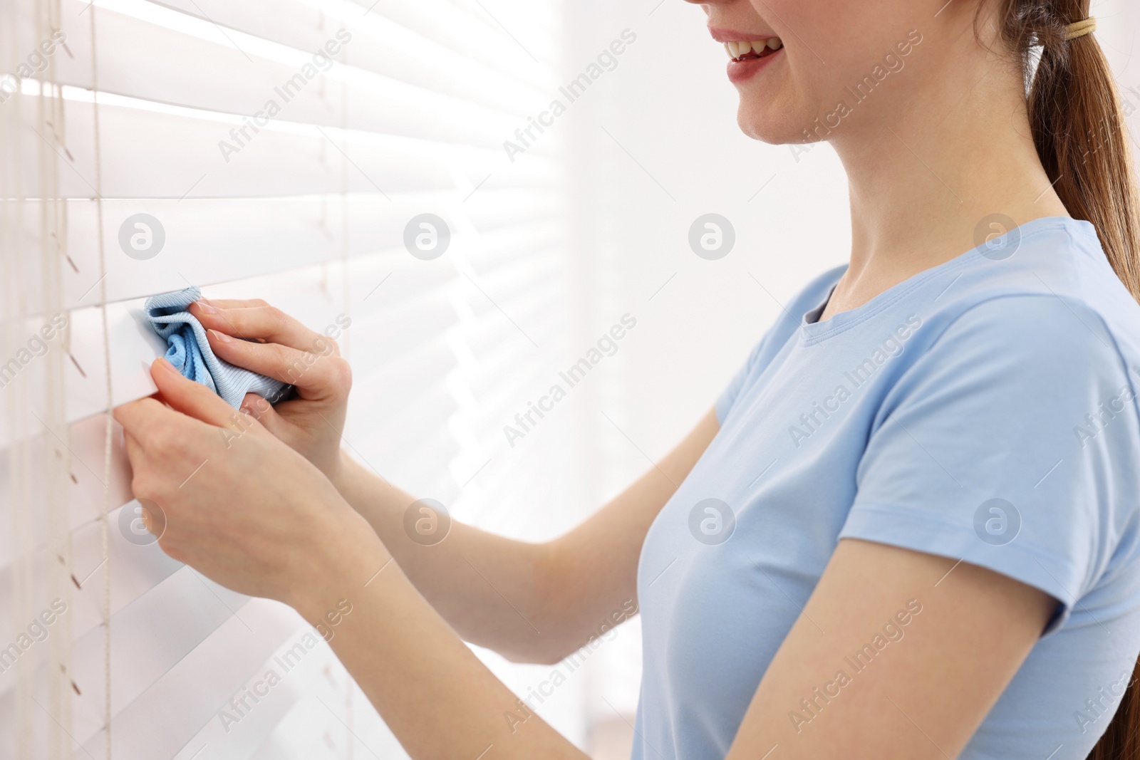 Photo of Woman with microfiber cloth wiping blinds at home, closeup