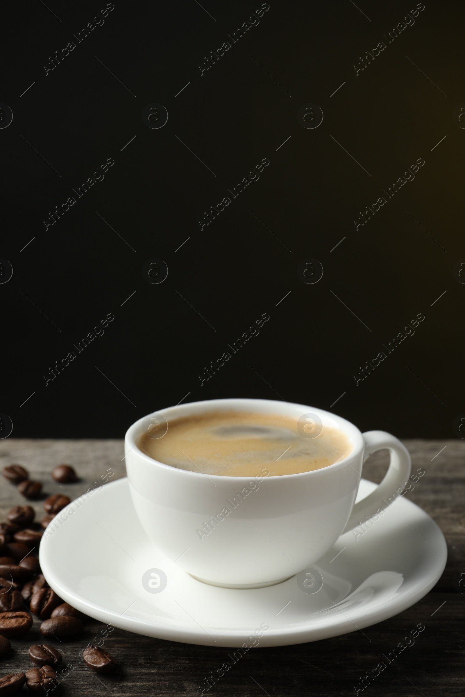 Photo of Cup of hot aromatic coffee and roasted beans on wooden table against dark background