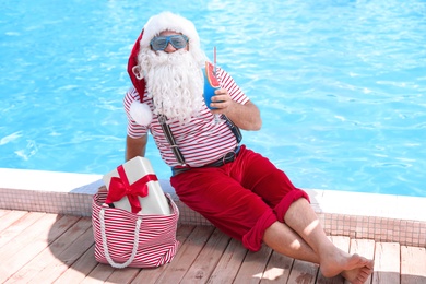 Photo of Authentic Santa Claus with cocktail and gift in bag near pool at resort