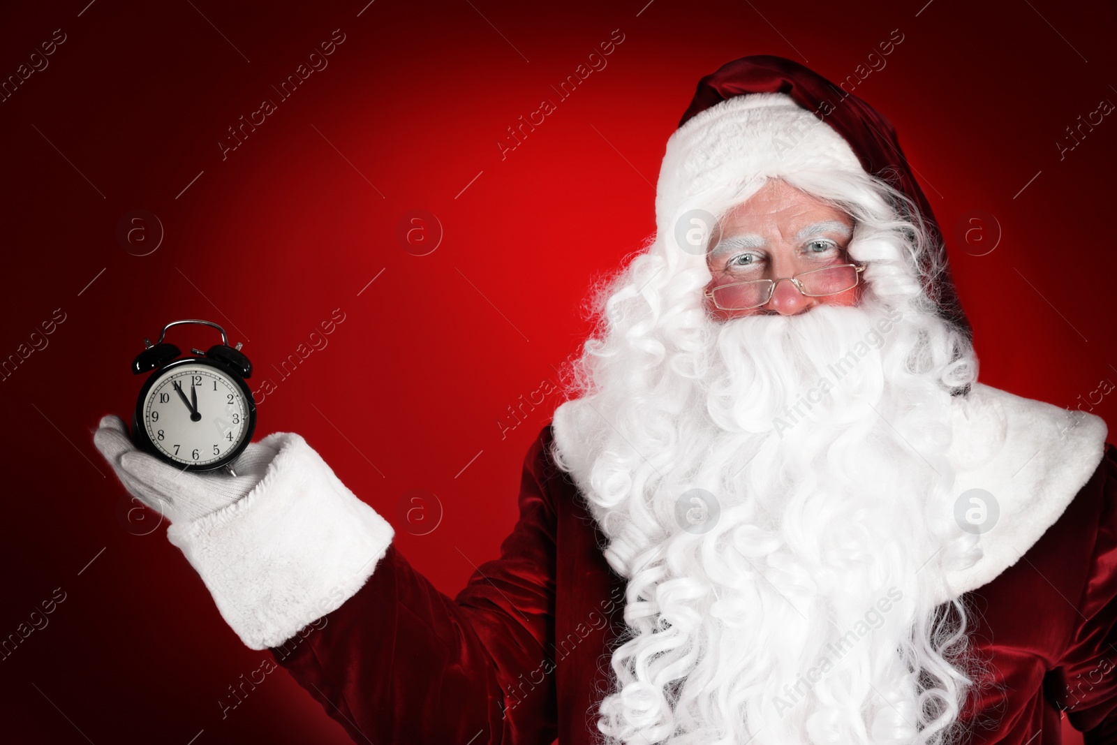 Photo of Santa Claus holding alarm clock on red background. Christmas countdown