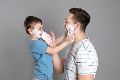 Photo of Dad and his little son having fun while applying shaving foam on color background