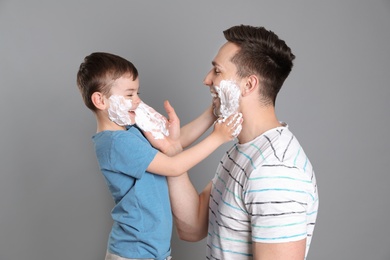 Dad and his little son having fun while applying shaving foam on color background