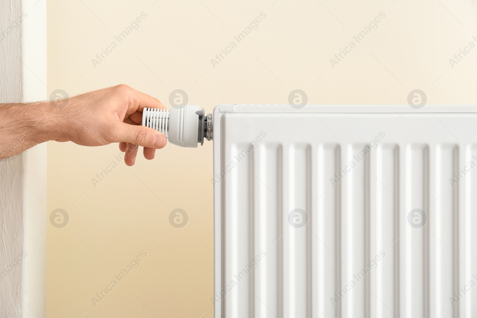 Photo of Man adjusting heating radiator thermostat indoors